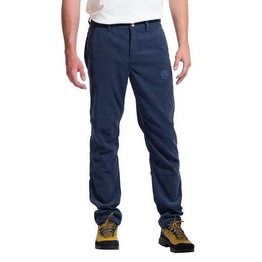 A person stands against a white background wearing a white shirt, La Sportiva Setter Pants Men's (blue with small logo on the left thigh), and yellow hiking boots—an ideal outfit for cold weather climbing. The person's head is not visible.