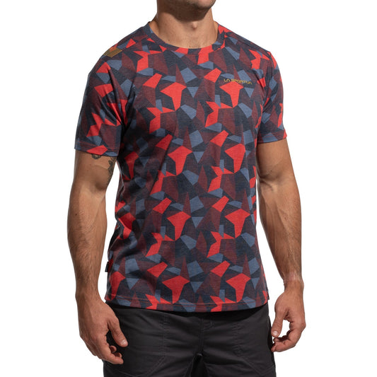 A person wearing the La Sportiva Dimension T-Shirt Men's (2025), made from recycled polyester with a red, blue, and black geometric pattern and dark shorts, stands against a white background. Their head is not visible in the image.