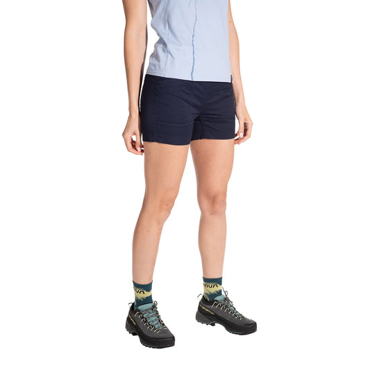 A person wears an athletic fit navy La Sportiva Joya Shorts Women's with a light blue shirt, patterned teal socks, and black hiking boots, standing against a white background. Their head and upper torso are not visible.