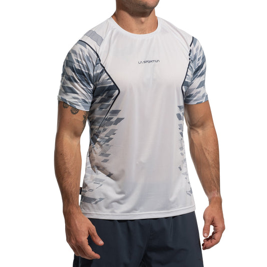 A man stands against a plain white background, wearing the La Sportiva Pacer T-Shirt Men's—an ultralight tee with a white and gray pattern made from recycled fabrics—paired with dark shorts. His face is not visible.