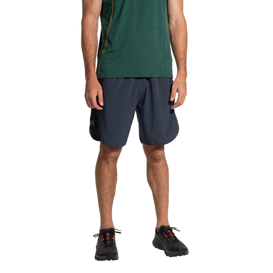 A person is wearing a green short-sleeve shirt, La Sportiva Sudden Shorts Men's navy running shorts with an 8" inseam, and black athletic shoes, standing against a white background. The head is not visible.