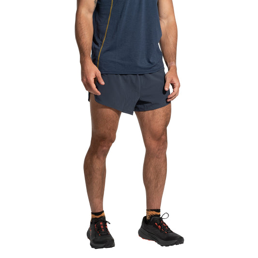 A person stands facing forward with arms relaxed by their sides, wearing a navy blue T-shirt, La Sportiva Auster Shorts Men's, patterned socks, and black athletic shoes. Their head is not visible in the image.
