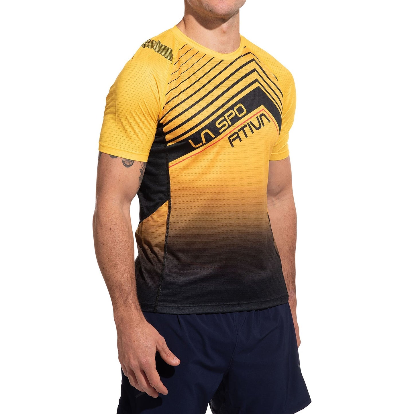 A man wearing the La Sportiva Wave T-Shirt Men's in a yellow and black gradient, paired with dark shorts, stands against a white background. The shirt displays "LA SPO ATTIV" text, and his head is not visible in the image.
