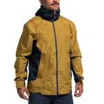 A man wears the La Sportiva Discover Shell Jacket Men's (2025) in mustard yellow and navy blue with red accents, an adjustable hood, front zipper, and stands with hands relaxed at his sides.