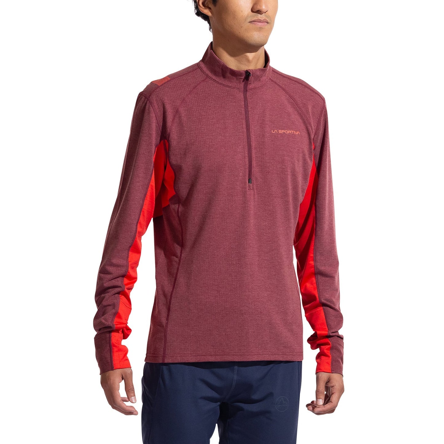 A man wearing the La Sportiva Swift Long Sleeve Men's shirt in maroon with red side panels and navy blue pants stands facing forward, arms relaxed—ideal attire for winter mountain running.