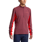 A man wearing the La Sportiva Swift Long Sleeve Men's shirt in maroon with red side panels and navy blue pants stands facing forward, arms relaxed—ideal attire for winter mountain running.
