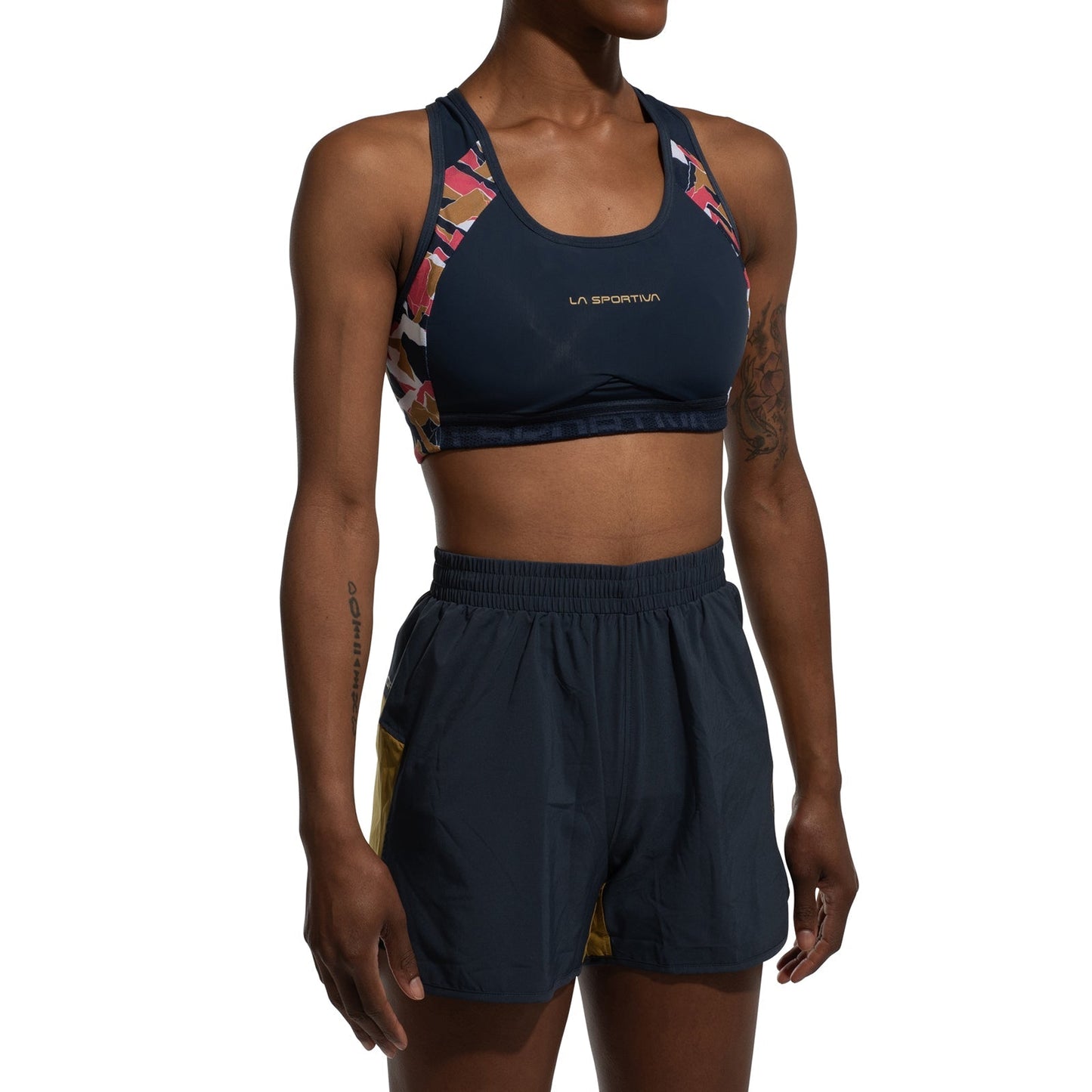 A person wearing the La Sportiva Hover Top Women's sports bra with colorful geometric straps and matching navy shorts with yellow side panels, standing against a white background.