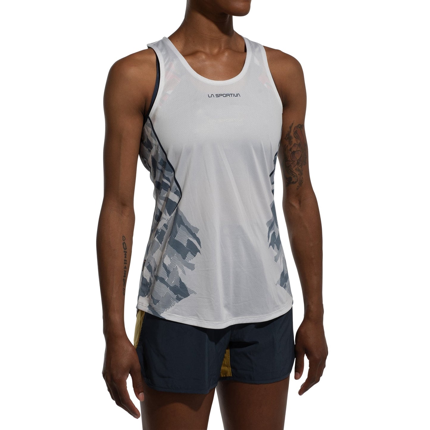 A woman in a white La Sportiva Pacer Tank Women's, featuring gray side patterns and made from recycled polyester, paired with black and yellow running shorts, stands against a white background.