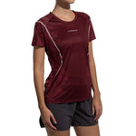 A woman wearing the La Sportiva Pacer T-Shirt Women's in maroon with white accents and black shorts stands against a white background. The shirt features "La Sportiva" text on the chest.