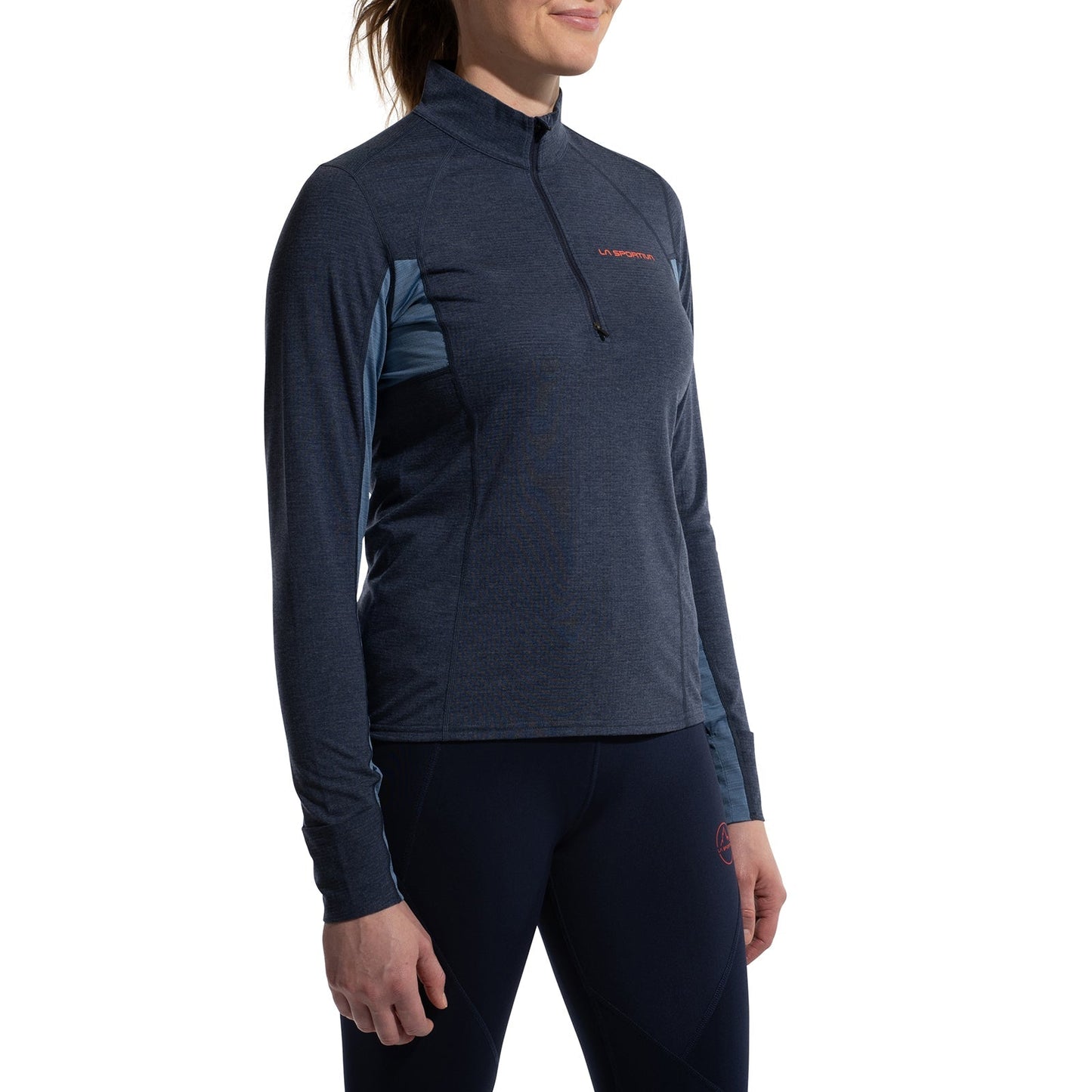 A woman in La Sportiva's Swift Long Sleeve, a navy-blue technical pullover with matching leggings, stands against a white background—ideal winter wear for mountain running.