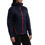Wearing the La Sportiva Ethereal Pro Jacket Women's in navy blue with a bright red zipper and logo, paired with black leggings featuring pink accents, a woman stands against a white background.