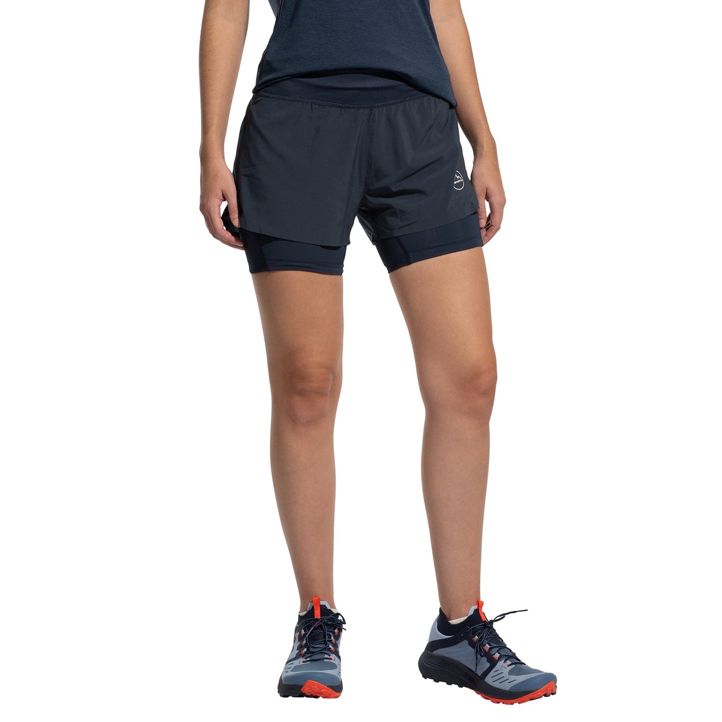 A person stands against a white background wearing a dark blue T-shirt, La Sportiva Ultra Distance Shorts Women's, and navy-blue trail running shoes with orange accents. The person's head is not visible.