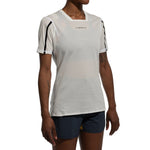 A woman wears the La Sportiva Trail Bite T-Shirt, a white, feather-light mesh trail running top, paired with dark blue shorts. She stands with arms relaxed against a plain white background.