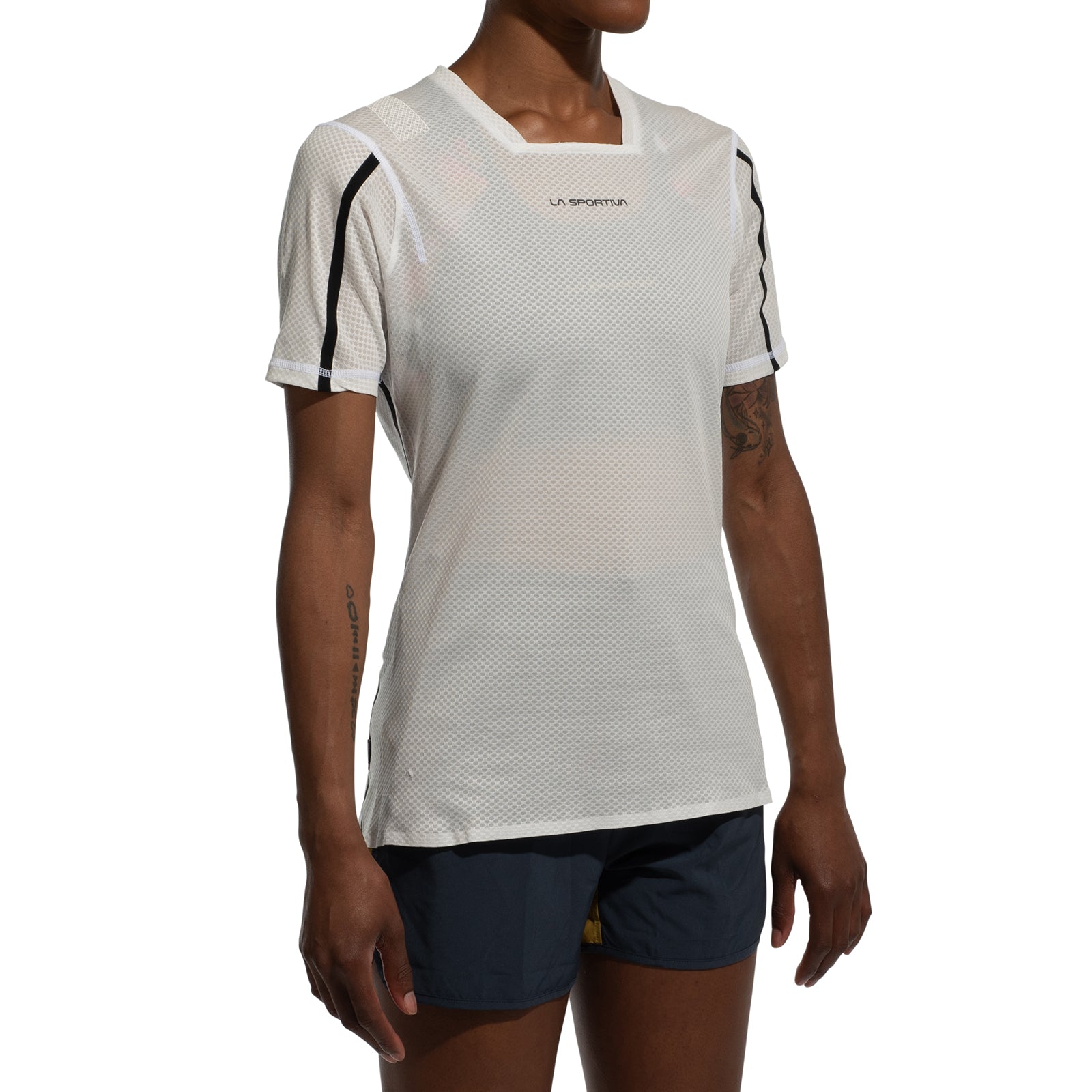 A woman wears the La Sportiva Trail Bite T-Shirt, a white, feather-light mesh trail running top, paired with dark blue shorts. She stands with arms relaxed against a plain white background.