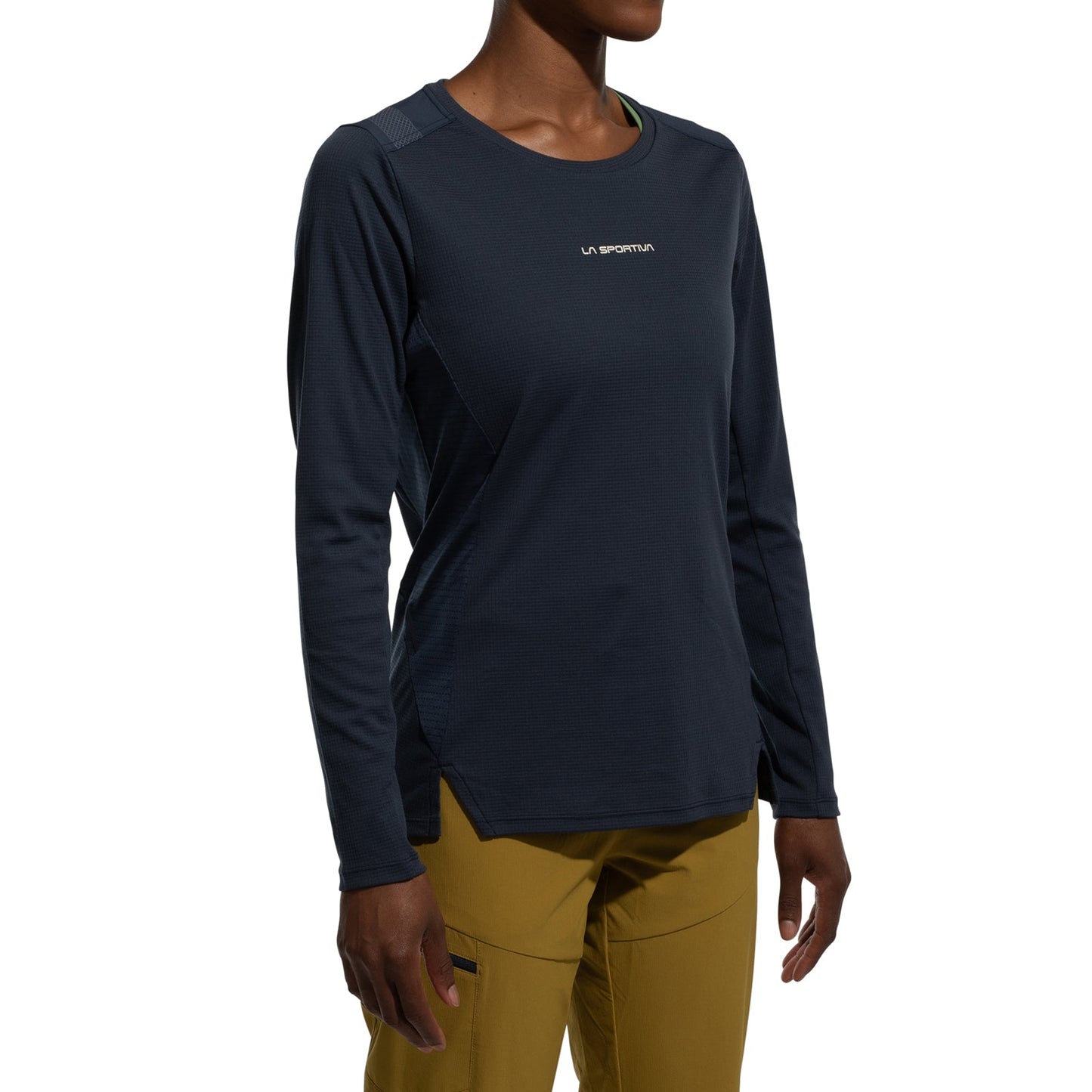 A woman wears the La Sportiva Beyond Long Sleeve Women's (2025) in dark blue Polartec Delta Cooling Fabric and mustard yellow pants, standing against a plain white background.