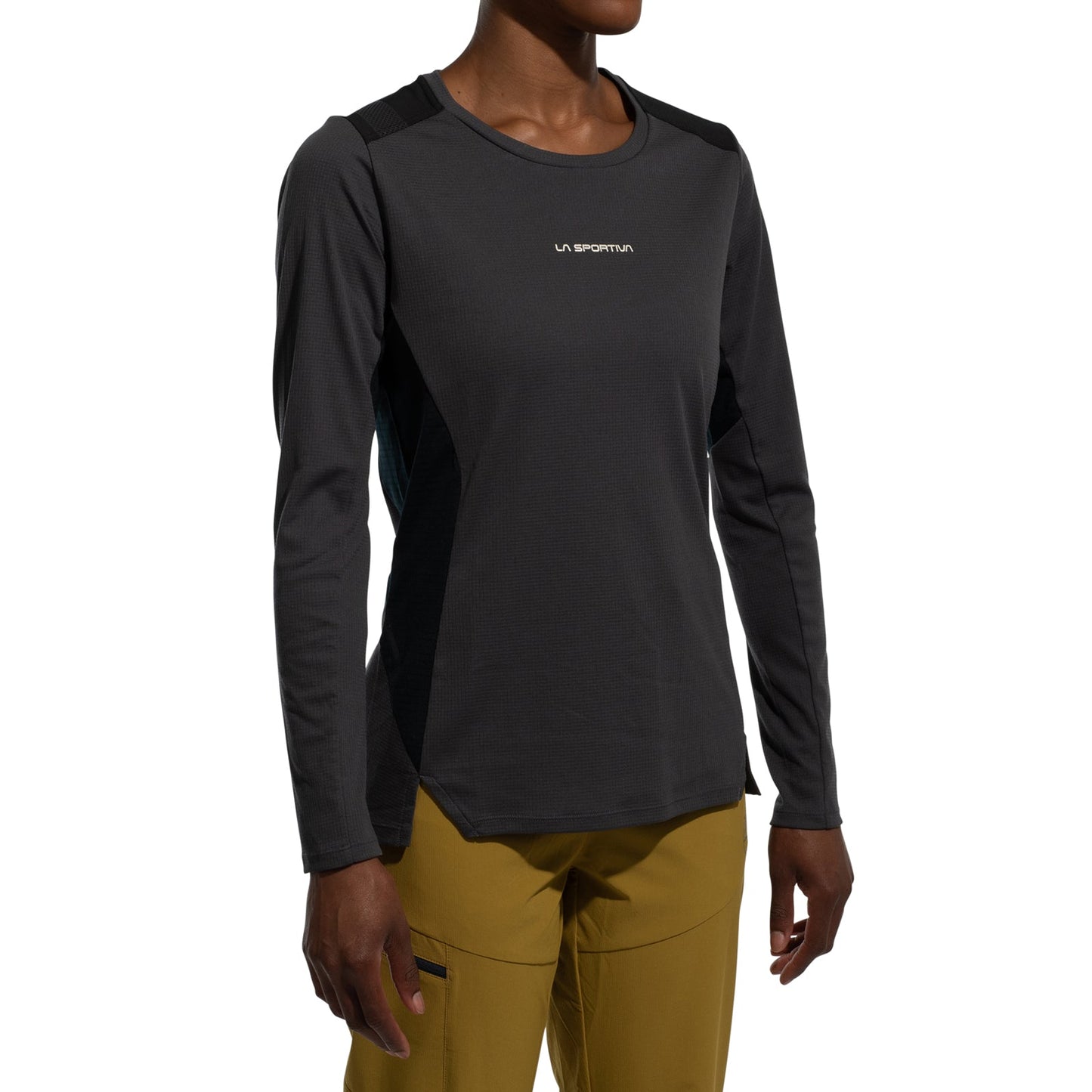 A woman wears the La Sportiva Beyond Long Sleeve Women's (2025) top with black shoulder panels and a chest logo, paired with mustard-yellow pants, standing against a plain white background.