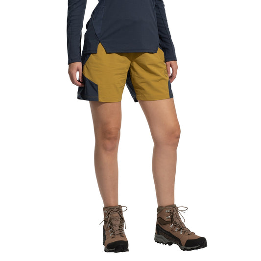 A person stands against a white background wearing La Sportiva Trail Guard Shorts Women's (2025) in yellow and navy, a navy long-sleeve top, and brown hiking boots. The quick-drying shorts are ideal for fast-hiking. The person's head is not visible.
