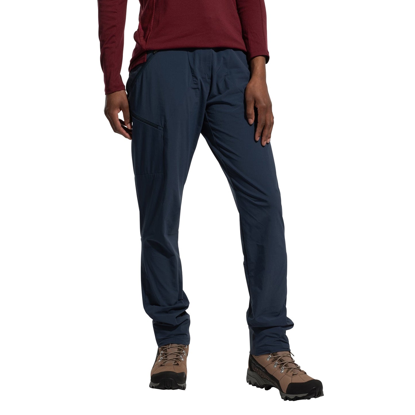 A person wearing a long-sleeve maroon shirt, brown hiking boots, and La Sportiva Monument Pants Women's (2025) stands with one hand on their thigh against a white background.