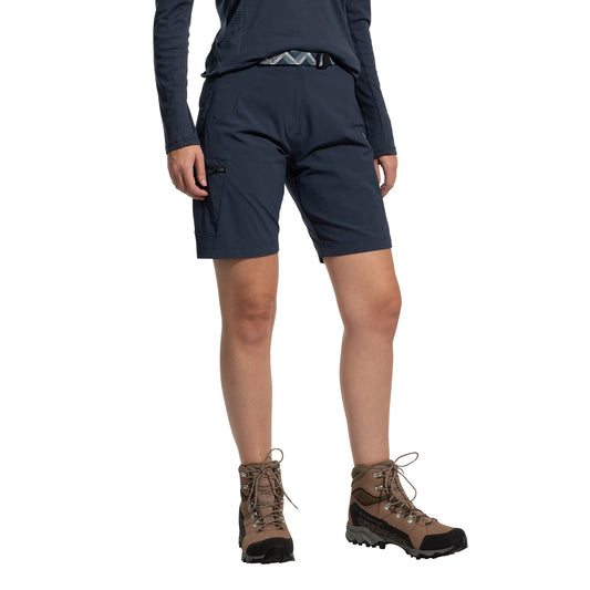 A person stands against a white background wearing La Sportiva West Crest Shorts Women's (2025) in navy blue, paired with a navy long-sleeve shirt, a patterned belt, and brown hiking boots. Their head is not visible in the image.