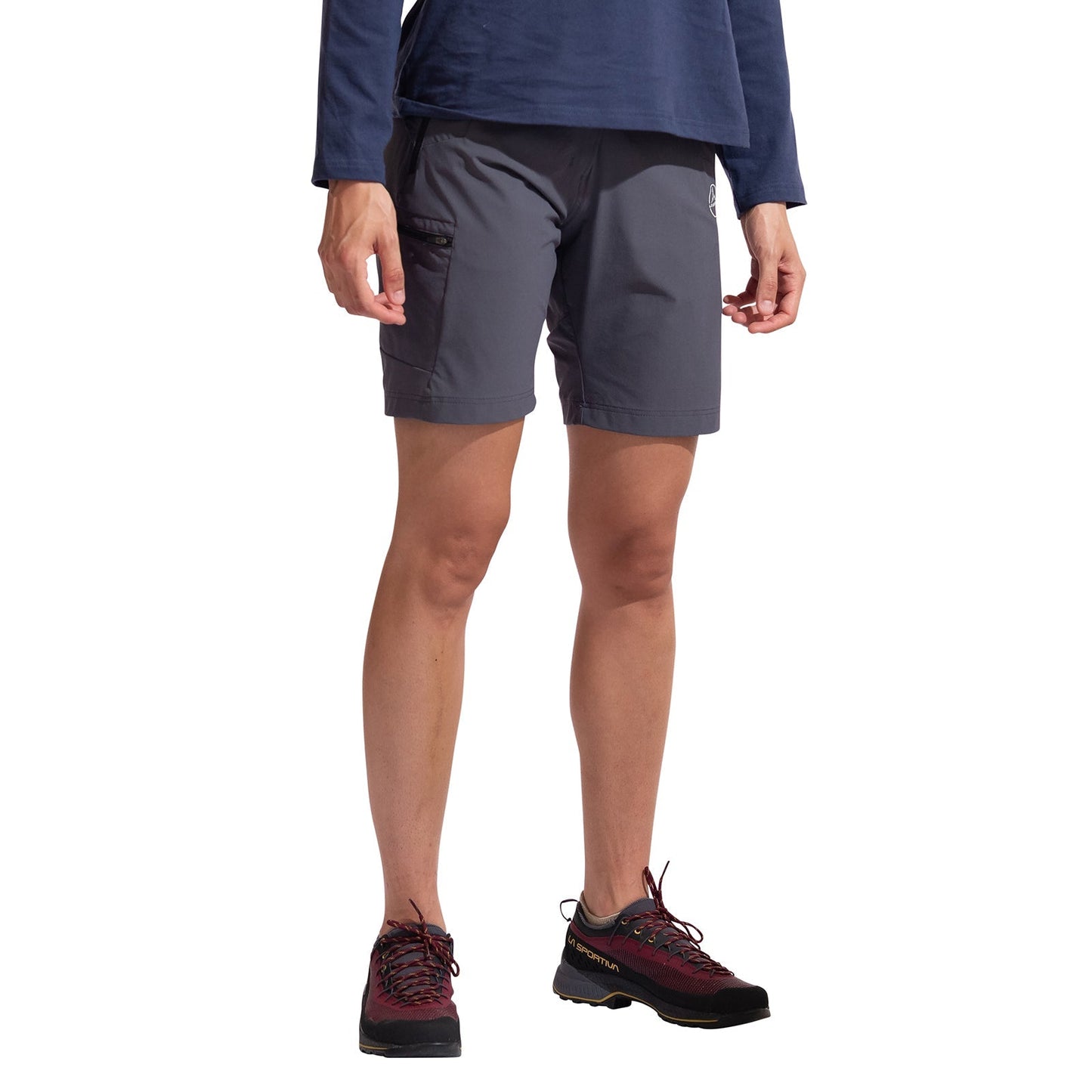 A person wearing a long-sleeve navy shirt, La Sportiva West Crest Shorts Women's (2025) in dark gray with a side pocket, and black-and-red hiking shoes stands against a plain white background.