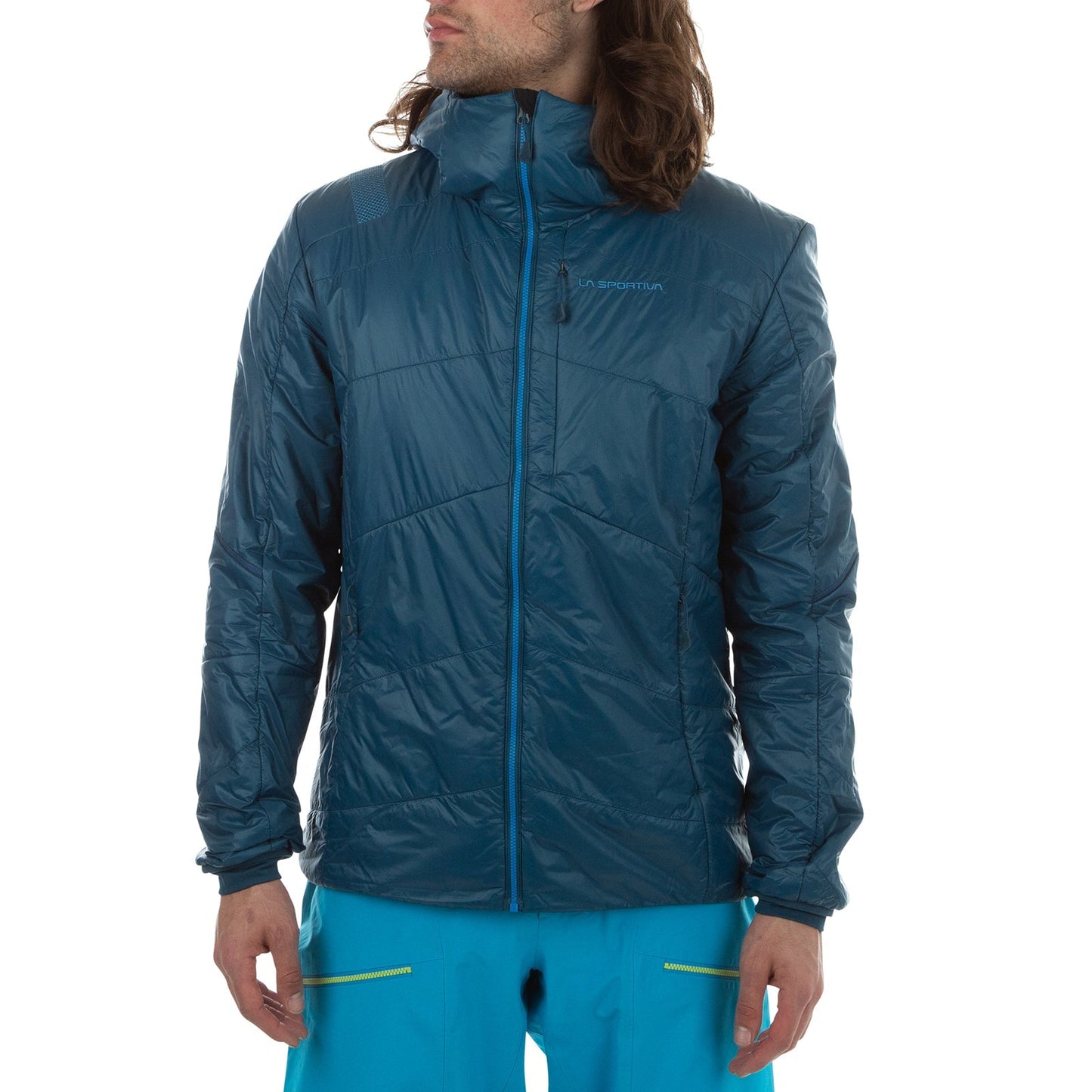 A man in a teal blue La Sportiva Alpine Guide Primaloft Hoody Men's (2024) with high collar and zippered chest pocket, plus bright blue pants, stands slightly turned against a plain white background. The jacket is lightweight and breathable.