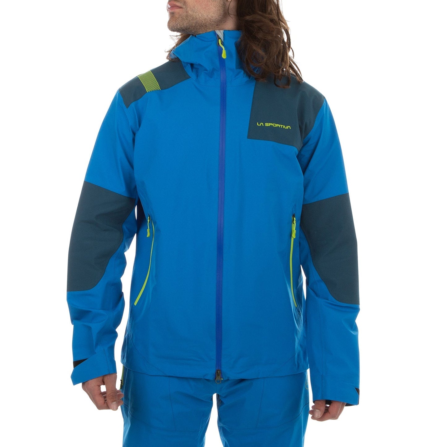 A person wears the La Sportiva Roseg GTX Jacket Men's in bright blue with dark gray accents and green zippers. The hardshell features a high collar and hood, partially covering their face beneath long brown hair.