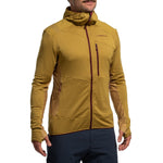 A person wears the La Sportiva Aequilibrium Thermal Hoody Men's (2025) in mustard yellow, featuring a chest zipper pocket, thumb holes, and subtle panel details, paired with dark blue pants—ideal as a fitted midlayer for outdoor adventures.