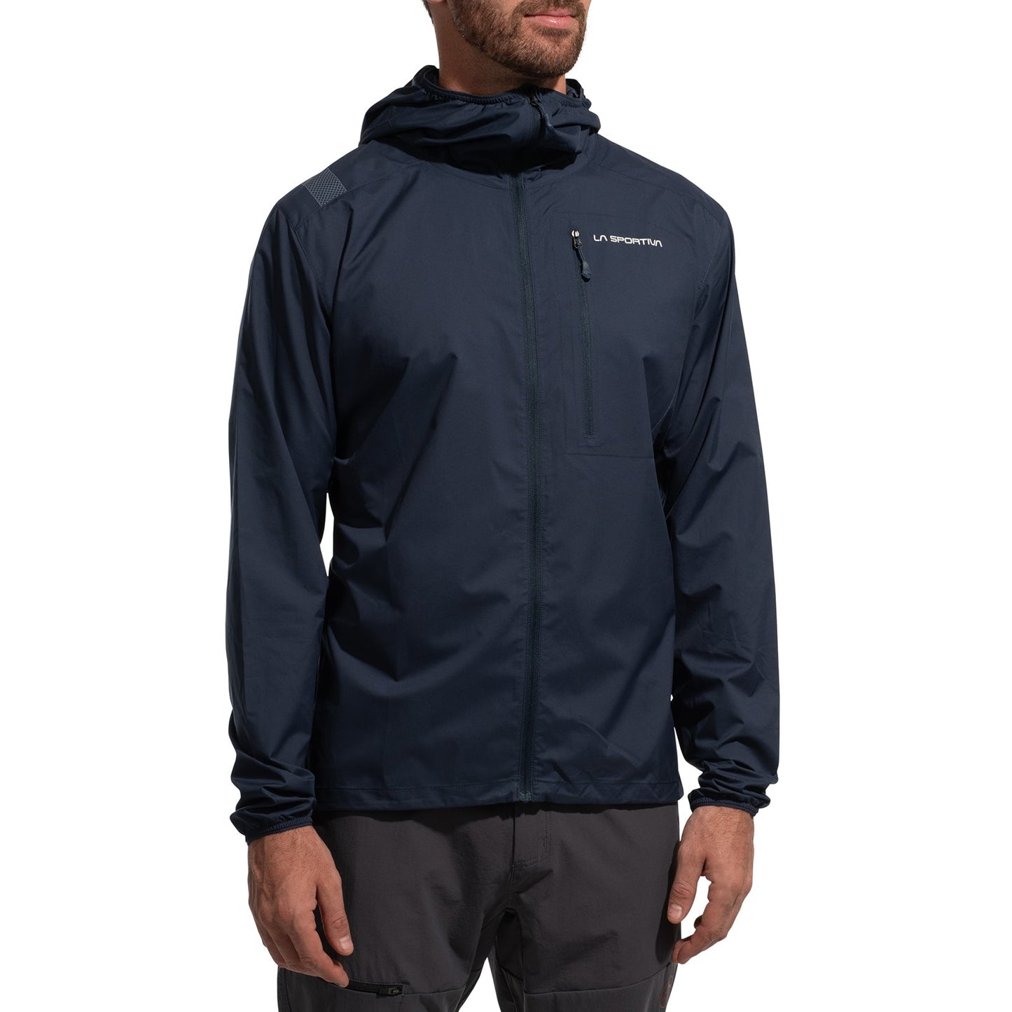 A person stands with arms relaxed, wearing the La Sportiva Wall Breeze Stretch Jacket Men's (2025) in dark navy blue. The alpine jacket features a front zipper, chest pocket, helmet-compatible hood, wind protection, and a small chest logo.