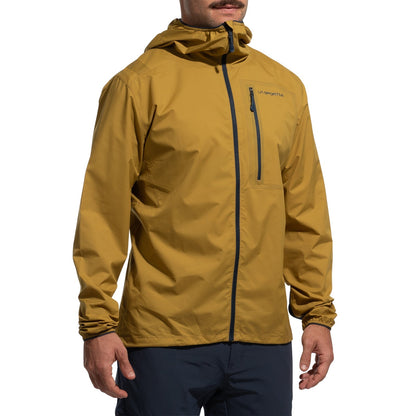 A man wearing the La Sportiva Wall Breeze Stretch Jacket Men's (2025) in mustard yellow, featuring wind protection, front zipper, chest pocket, elastic cuffs, logo on the left chest, helmet-compatible hood, and dark pants.