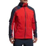 A person wearing the La Sportiva Aequilibrium Speed Jacket Men's (2025) in red and dark navy, featuring breathable fabric and black zippers, stands with hands relaxed by their sides against a plain white background, showing only torso and lower face.