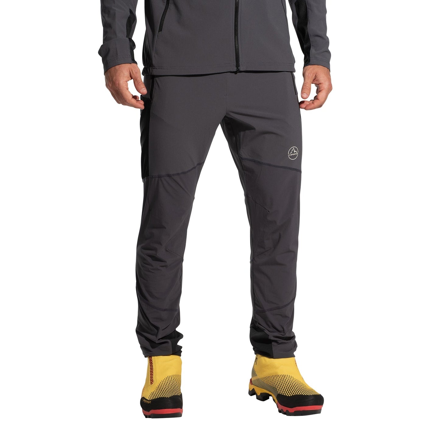 A person wearing La Sportiva Aequilibrium Speed Pants Men's (2025) in dark gray and a matching jacket, paired with bright yellow hiking boots with black and red soles. The wind-protective, quick-drying outfit is shown cropped from the shoulders down.
