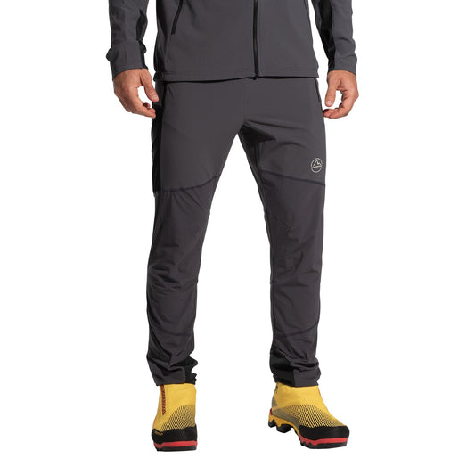 A person wearing La Sportiva Aequilibrium Speed Pants Men's (2025) in dark gray and a matching jacket, paired with bright yellow hiking boots with black and red soles. The wind-protective, quick-drying outfit is shown cropped from the shoulders down.
