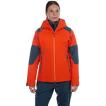 A person stands facing forward against a white background, wearing the La Sportiva Roseg GTX Jacket Women's in orange and gray, paired with blue pants.