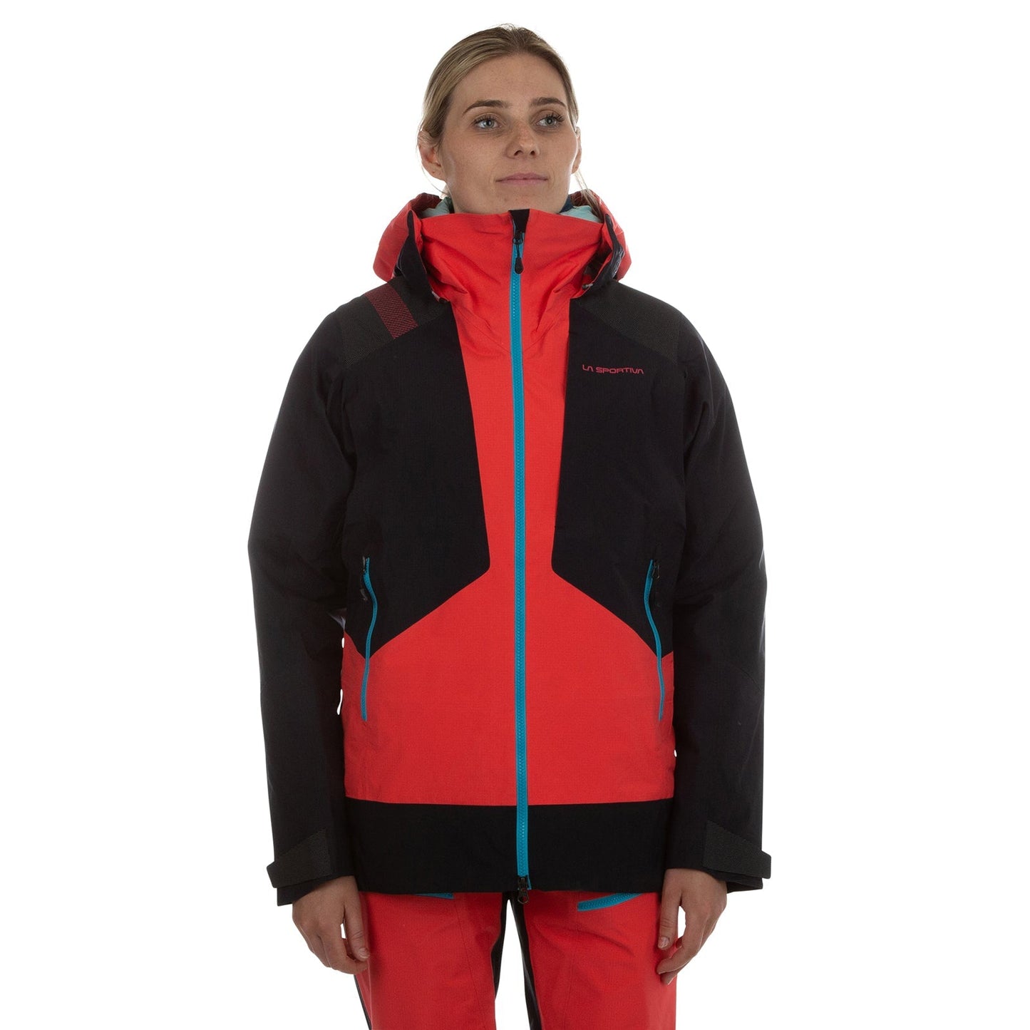 A woman faces forward in a La Sportiva Supercouloir GTX Pro Jacket Women's (2024) with red and black Gore-Tex PRO fabric, turquoise zippers, and matching red pants, standing against a white background ready for winter activities.