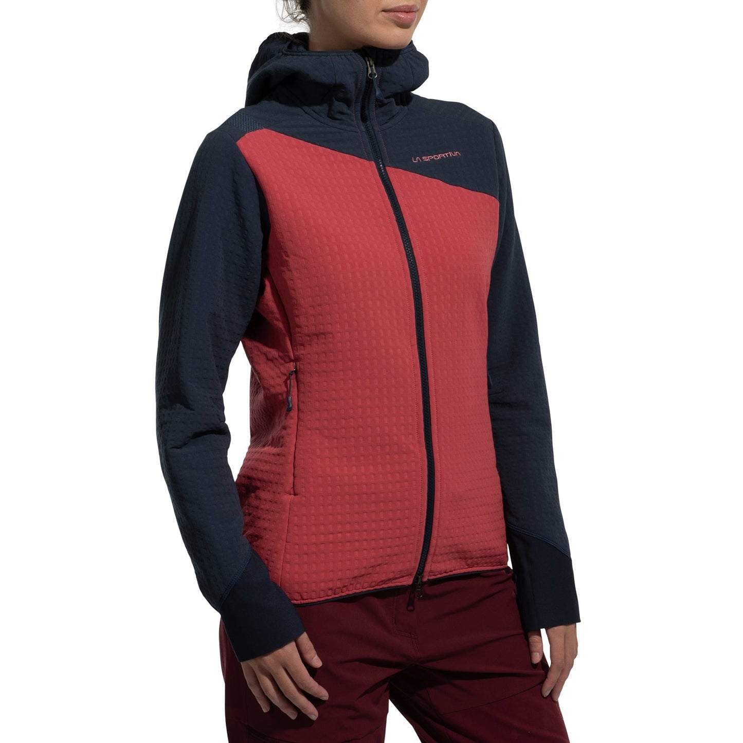 A woman wearing the La Sportiva Bristen Thermal Hoody Women's, a red and navy blue fleece with a textured pattern ideal for outdoor activities, stands against a plain white background.