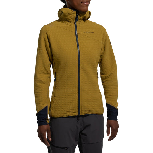 A person wears the La Sportiva Bristen Thermal Hoody Women's in mustard yellow, a textured, hooded fleece with zippered front and pockets, plus black trimmed cuffs—ideal for outdoor activities—paired with gray pants. The face is partially out of frame.