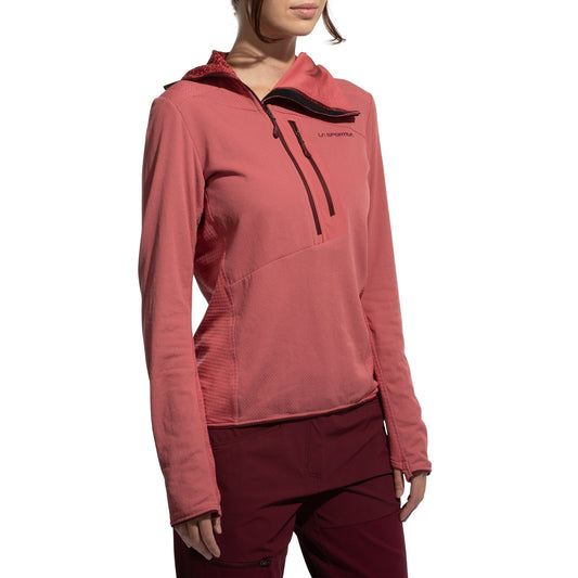 A person wears the La Sportiva Big Wall Pullover Hoody Women's (2025) in coral pink with long sleeves, a half-zip, chest logo, TechStretch Aero Fabric with Polartec inserts, fitted design, and matching burgundy pants against a white background.