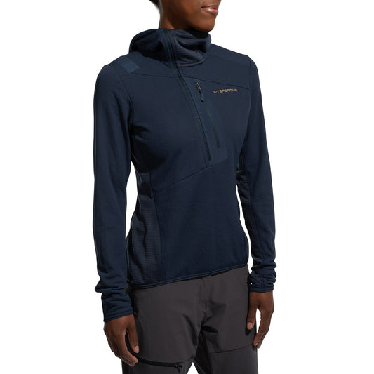 A woman stands with hands by her sides against a plain white background, wearing the La Sportiva Big Wall Pullover Hoody Women's (2025) in navy blue and gray pants. The hoody features TechStretch Aero Fabric, Polartec inserts, and a chest pocket.