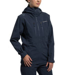 A woman stands against a plain white background, hands by her sides, wearing the La Sportiva Helixir Shell Jacket Women's (2025)—a dark blue, waterproof jacket with zippered chest pockets and matching pants, ideal for big wall adventures.