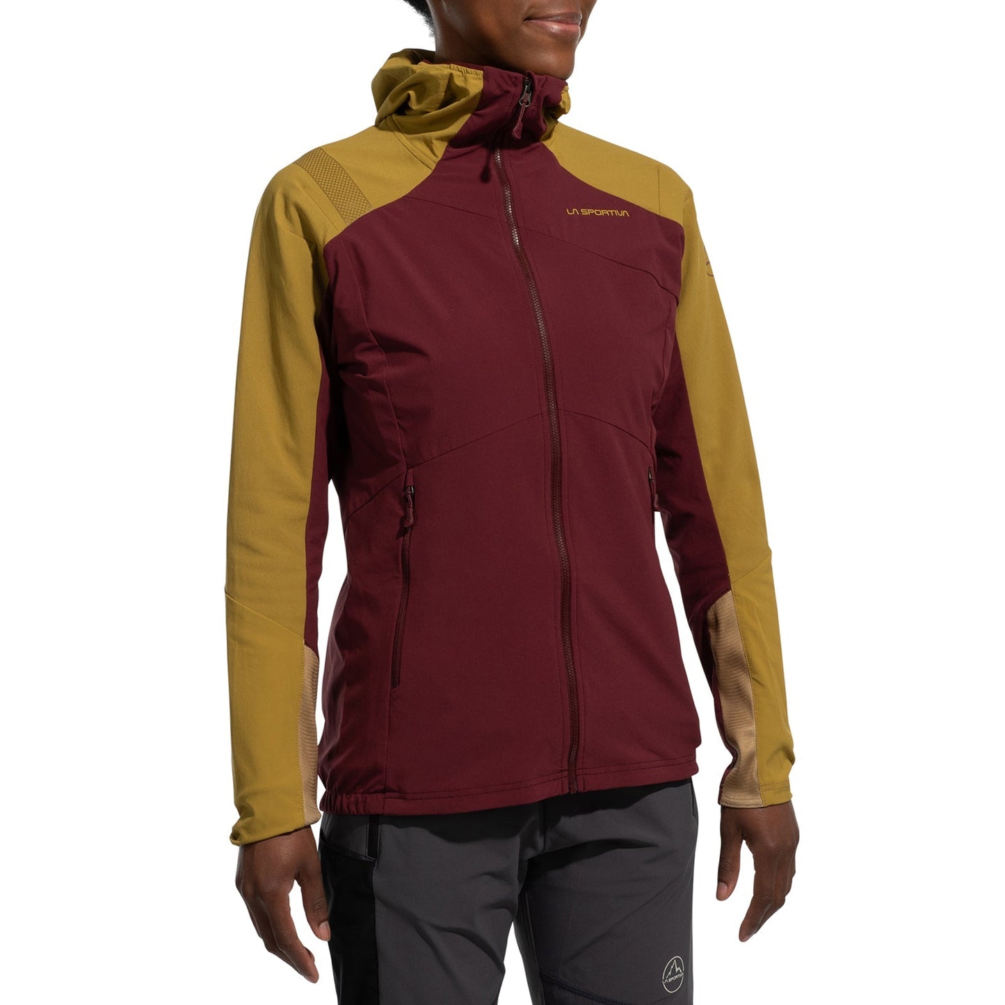 A person wears the La Sportiva Aequilibrium Speed Jacket Women's (2025), a two-tone hooded jacket with maroon body and mustard yellow sleeves, made from breathable fabric for lightweight warmth, paired with gray pants against a plain white background.