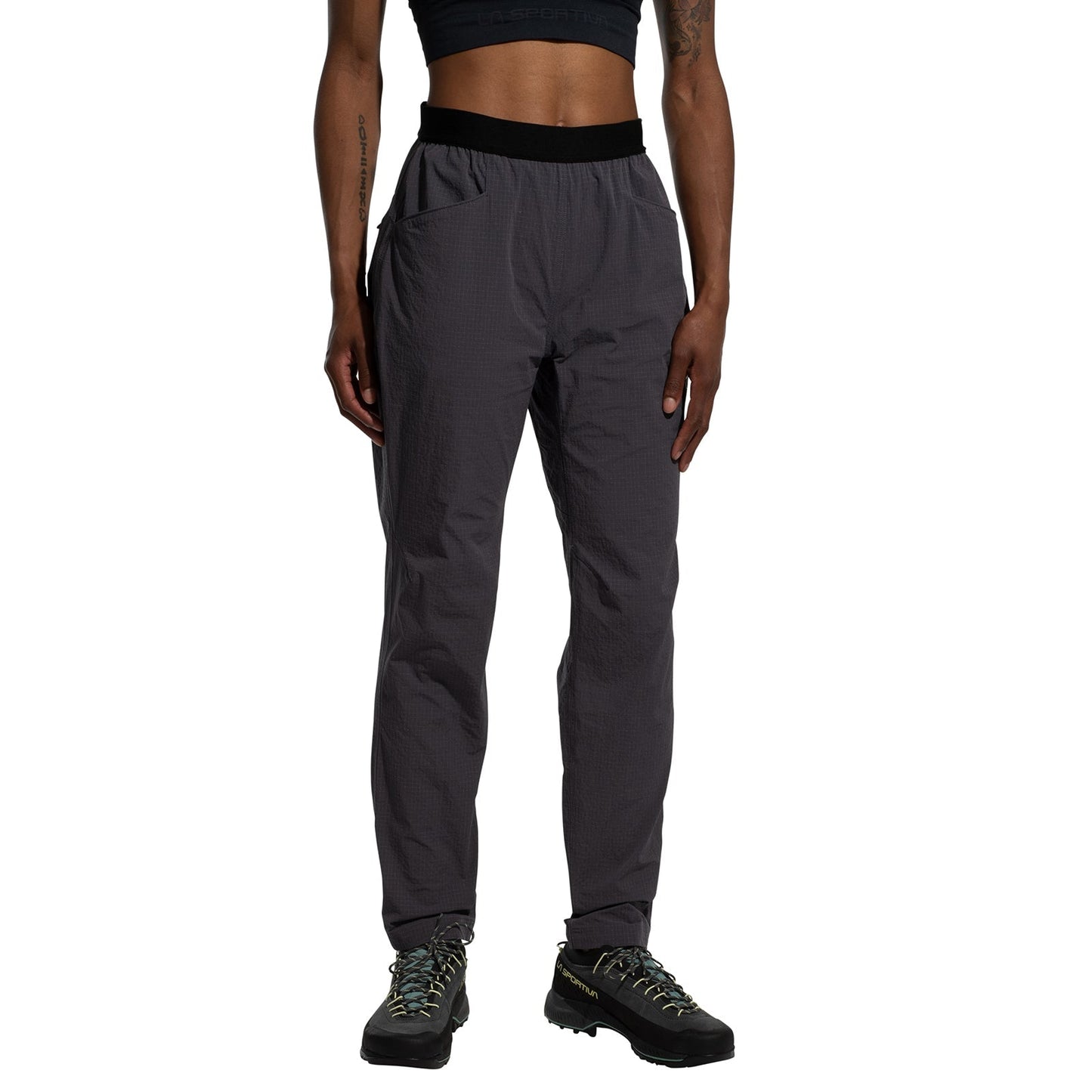A person is wearing a black crop top, La Sportiva Helixir Pants Women’s (2025) made with durable Spectra® fibers and pockets, plus hiking shoes, against a white background. Only their torso and legs are visible.