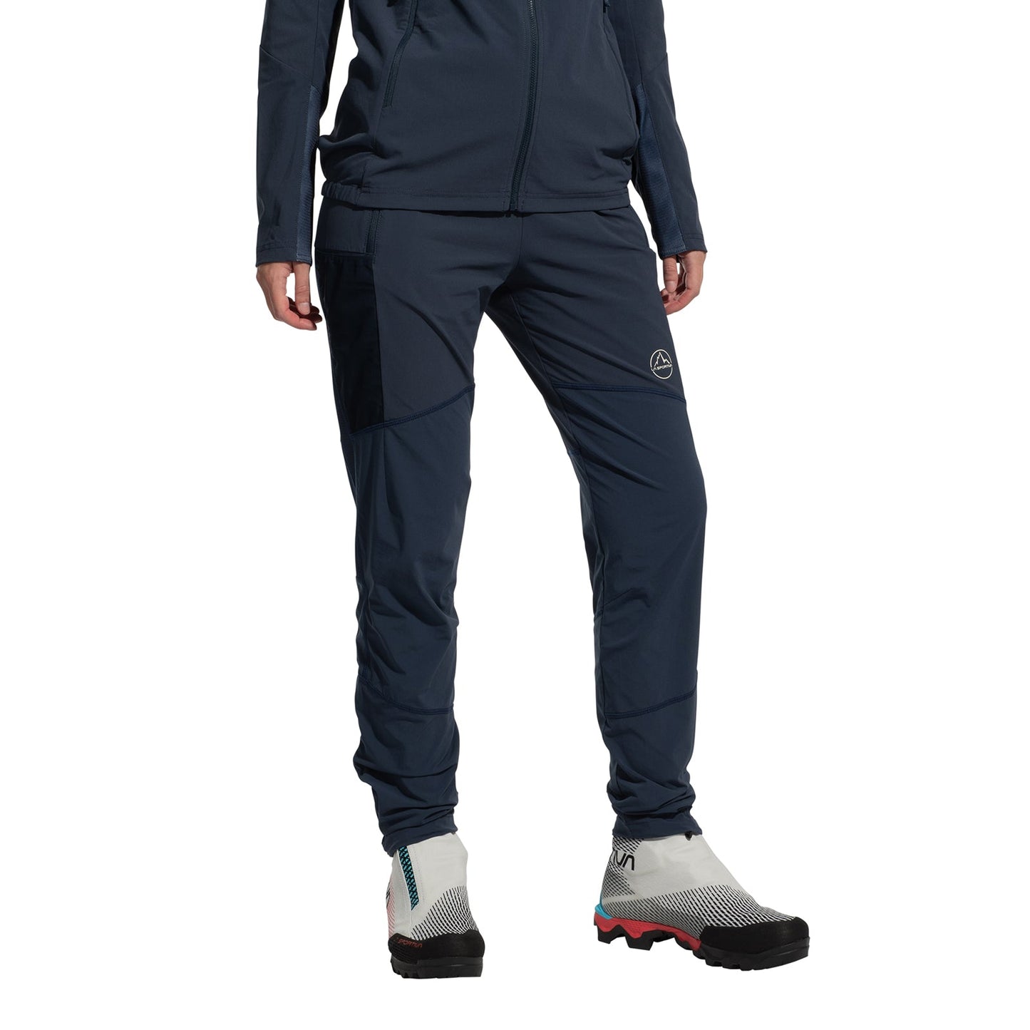 A person models La Sportiva’s Aequilibrium Speed Tights Women’s in navy blue with a matching jacket and white trail running shoes (black toes, red soles) against a plain white background. Their face is not visible.