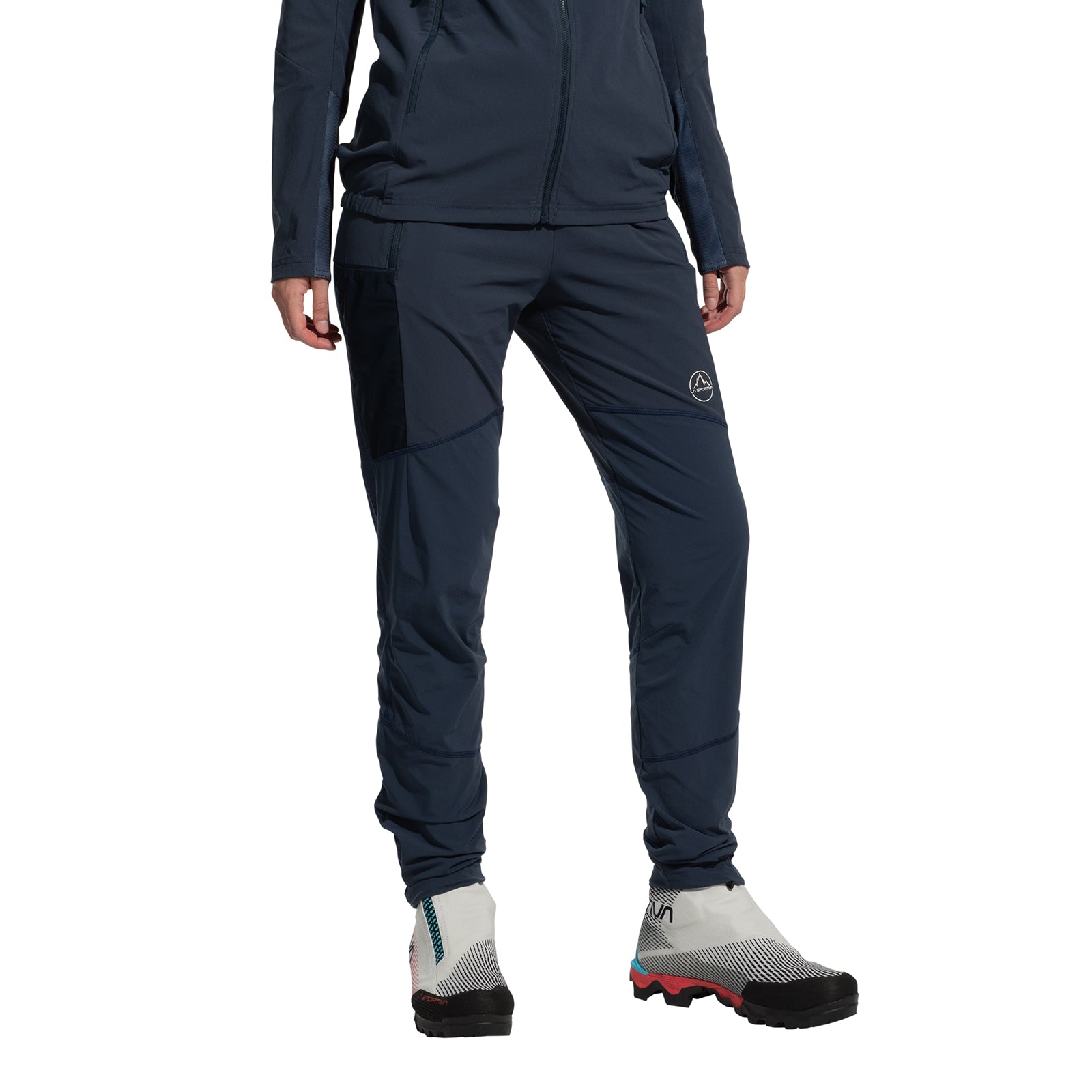 A person models La Sportiva’s Aequilibrium Speed Tights Women’s in navy blue with a matching jacket and white trail running shoes (black toes, red soles) against a plain white background. Their face is not visible.