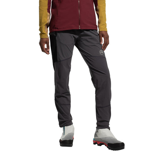 A person in a maroon and yellow jacket, La Sportiva Aequilibrium Speed Tights Women's (abrasion-resistant gray), and white trail running shoes with black and red soles stands against a plain white background.