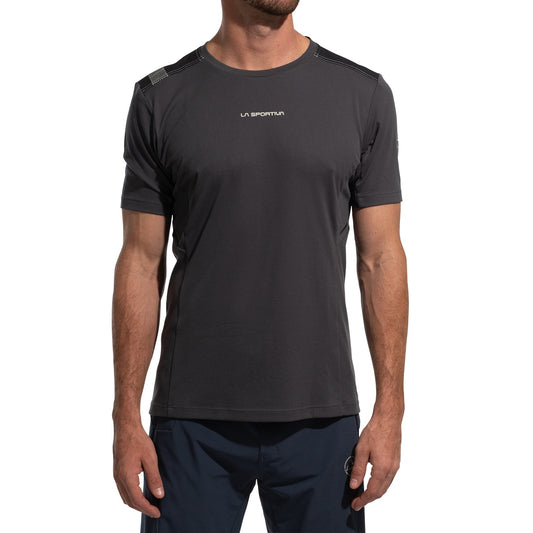 A man wears a dark gray La Sportiva Ridge T-Shirt Men's (2025) with navy shorts, standing against a white background. Only his upper body is shown, and his face is partially out of frame.