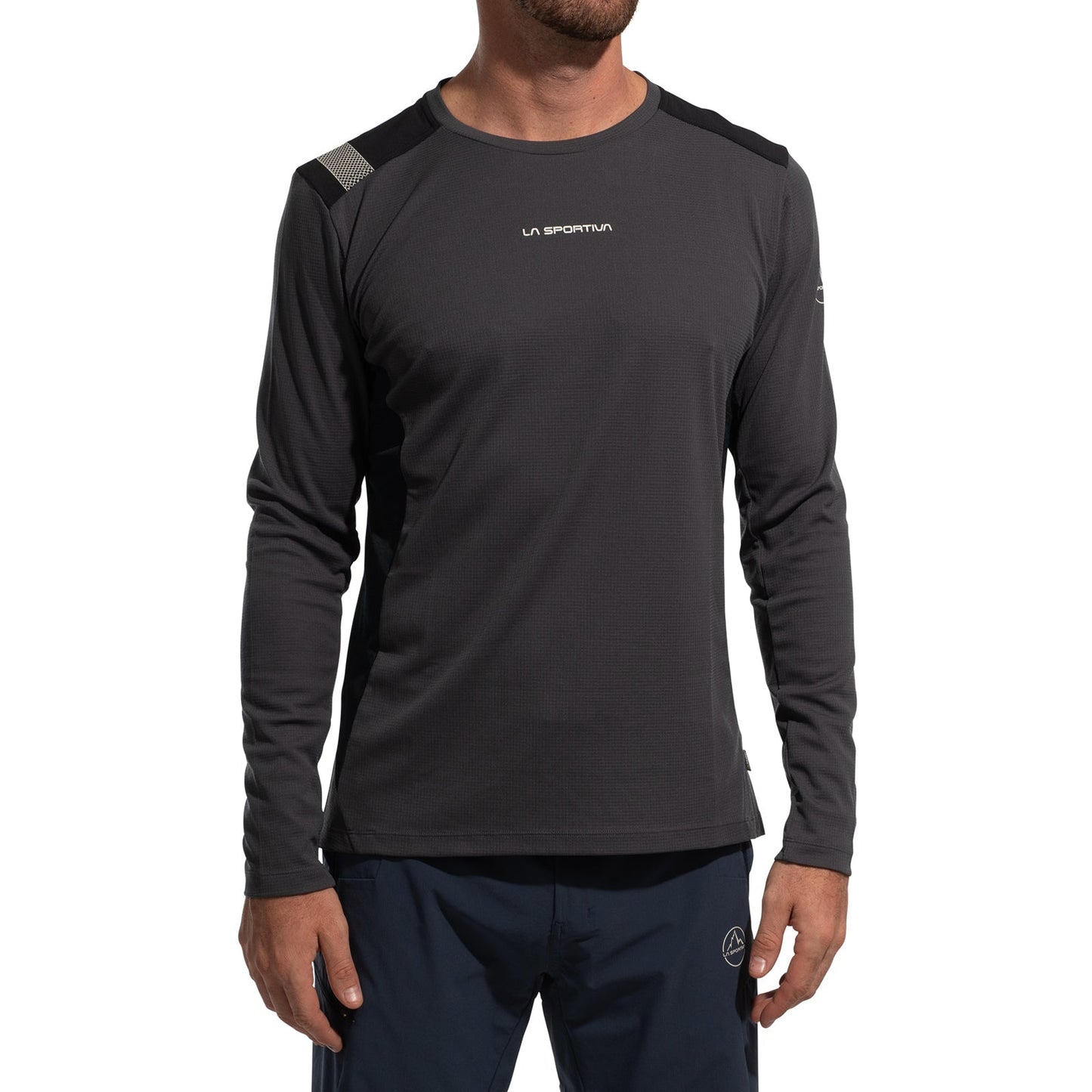 A man wears the La Sportiva Beyond Long Sleeve Men's (2025) top in dark color, featuring Polartec Delta Cooling Fabric, a chest logo, slim fit, and subtle shoulder details, paired with navy athletic pants. His head is not visible.
