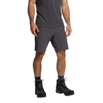 A man stands against a white background wearing La Sportiva Trail Guard Shorts Men's in dark grey, a matching quick-drying T-shirt, black hiking boots, and dark socks. His head is not visible in the image.