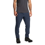 Man wearing a short-sleeve, dark gray breathable athletic shirt, La Sportiva Trail Guard Pants Men's (2025) in navy blue, and black hiking shoes, standing against a white background.