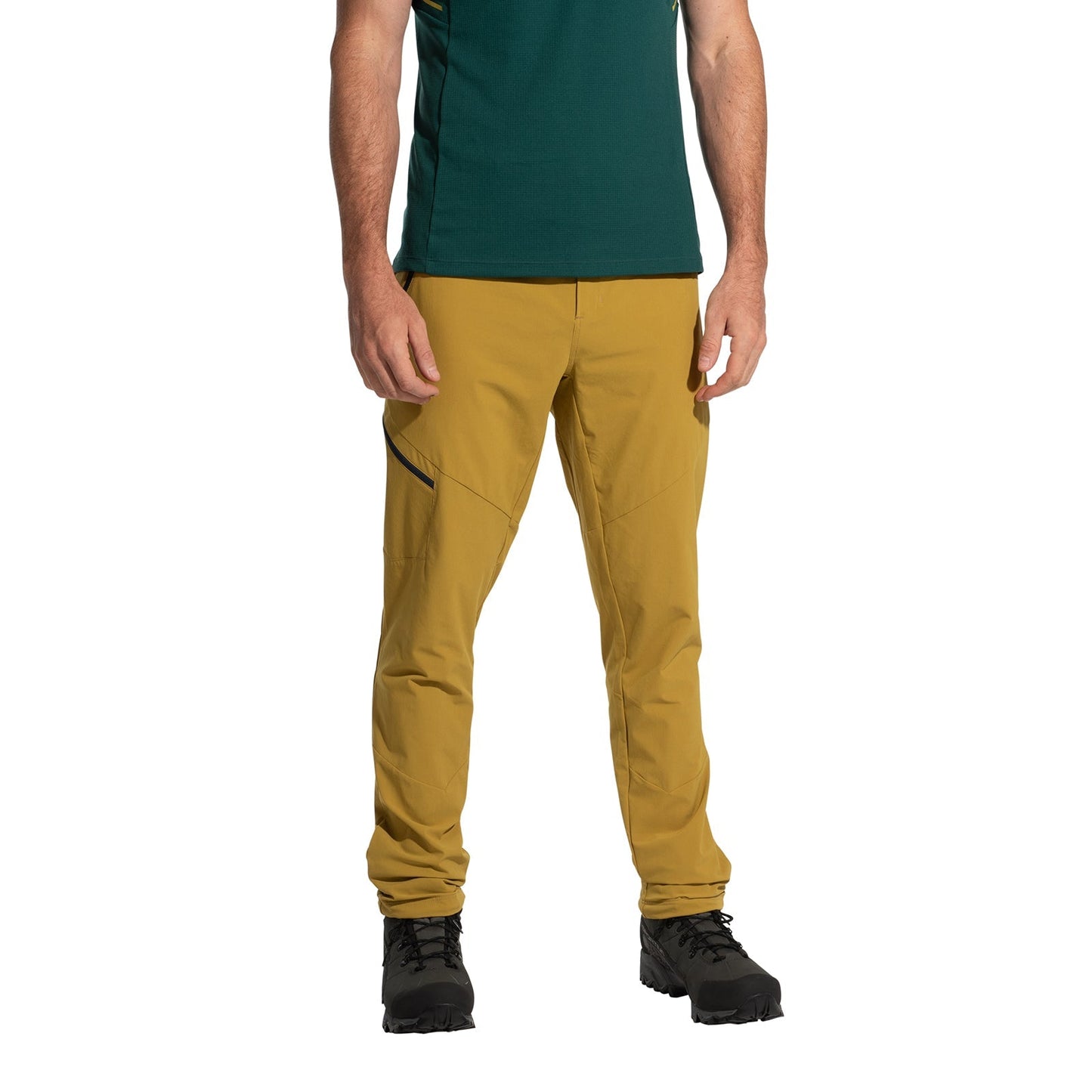 A person wears La Sportiva West Crest Pants Men's (2025) in mustard yellow with zippered pockets, paired with a green short-sleeve shirt and black hiking boots, standing against a white background. The photo is cropped at the shoulders.