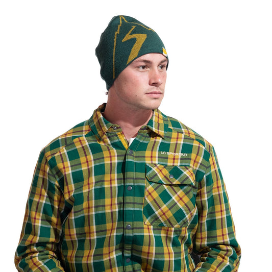 A man wearing a green and yellow plaid button-up shirt and the La Sportiva Woolly Beanie with a yellow lightning bolt, looking to the side against a white background—ideal for cold weather and comfort.